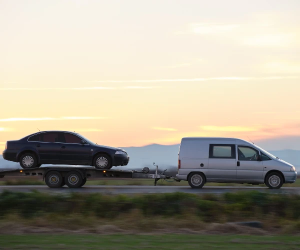 Tow truck vehicle with car transporting carrier trailer driving on highway in evening